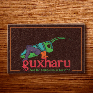 Aplicación del logo de Guxharu en una tarjeta sobre una mesa de madera